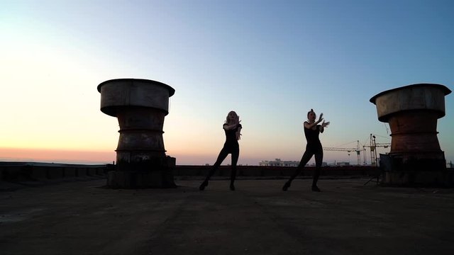 silhouettes of women dancing at sunset on roof with rainbow on background