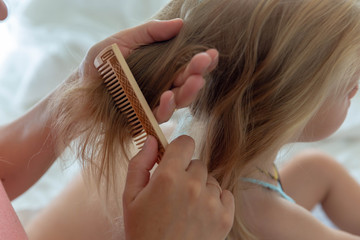 Women's hands comb the Golden hair of a little girl with a wooden comb.