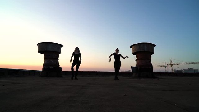silhouettes of dancers in bodysuits on roof against light sky with rainbow