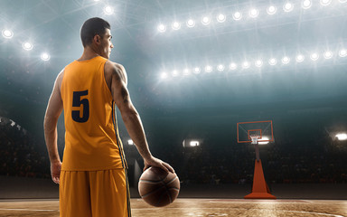 Professional basketball player in sports uniform on floodlit basketball court with a ball. View...