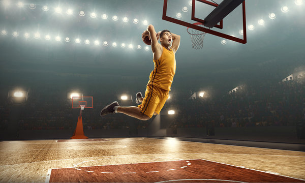 Basketball player scoring a slam dunk basket. Floodlit basketball court