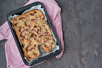 Sponge cake with plum and shtrezel in a black baking dish on a dark concrete background. Harvest plums. Recipes with plums. German food. Top view, copy space.