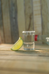 Detail of a shot of delicious tequila with a slice of lemon, salt and a bottle of tequila on a...