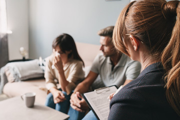 Photo of caucasian unhappy couple having conversation with psychologist on therapy session in room