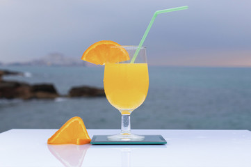 Glass with delicious orange juice and two slices of ripe orange and sea background
