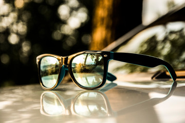 Sunglasses on a the hood of a car with the reflection of a beautiful scenery