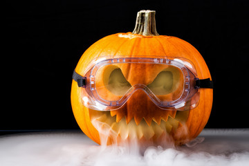 Halloween pumpkin with scary face on black background. Jack o lantern wearing laboratory glasses...