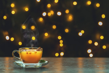 Obraz na płótnie Canvas Cup of hot spicy tea with yellow orange barries on dark Christmas and New Year background with light bokeh.