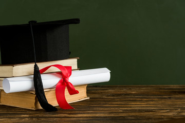 Mortarboard, textbooks and graduation scroll tied with red ribbon
