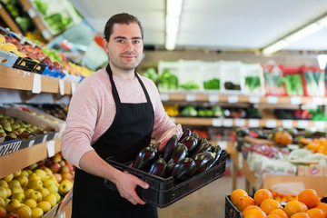 Salesman having tray of  eggplants on the supermarket