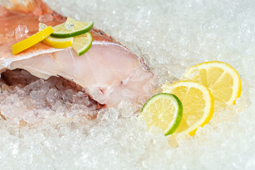 fresh sea ocean red perch fish, lying on ice, headless, cherry, sliced lemon and lime sliced round,...