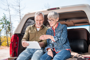 smiling senior couple sitting in car and using digital tablet in sunny day