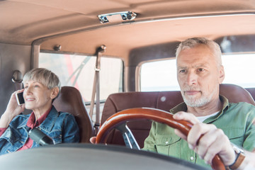 senior woman talking on smartphone while husband driving car