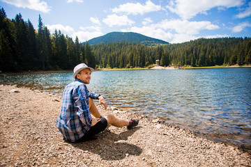 Traveler man in hat relaxing meditation with serene view mountains and lake landscape. Travel lifestyle hiking concept, summer vacations outdoor