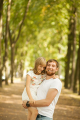 Fototapeta premium Portrait of lovely smiling daughter in her father's arms walking at green park outside. Happy family people concept