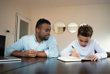 Mixed family at home. African father and african american child. dad helping son with school homework. Education and relationship, man teaching and boy learning. home schooling.