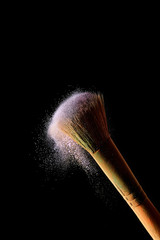 cosmetic brush with colorful violet powder on black background