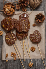 Slices of apples in chocolate, caramel glaze and walnuts on skewers on a dark background