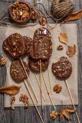 Slices of apples in chocolate, caramel glaze and walnuts on skewers on a dark background