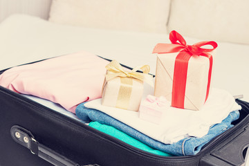 Fototapeta na wymiar Open suitcase with of clothes and two gift, closeup, cropped image, toned