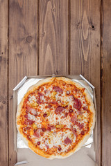 Italian pizza in cardboard box on wooden table. Top view