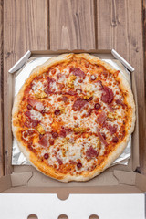 Italian pizza in cardboard box on wooden table. Top view