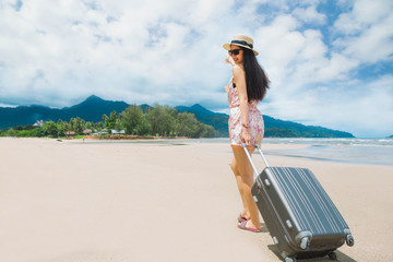 woman travel with a suitcase on the beach,  woman travel in hat with suitcase bag standing on the beach with the sea and blue sky background.