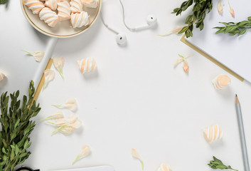 Fototapeta na wymiar Workspace with tablet, flower petals, pencil, green branches and marshmallows on white background. top view