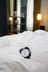Classic black alarm clock on the white wrinkled bed sheets