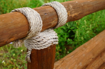 A thick, gray rope rope is wound on a brown log close-up, against a background of green grass.