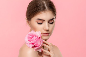Close-up portrait of a beautiful young girl with pink rose flower isolated over pink background.
