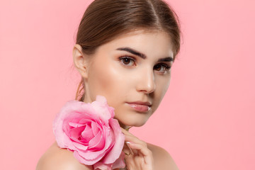 Obraz premium Close-up portrait of a beautiful young girl with pink rose flower isolated over pink background.