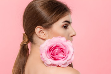 Close-up portrait of a beautiful young girl with pink rose flower isolated over pink background.