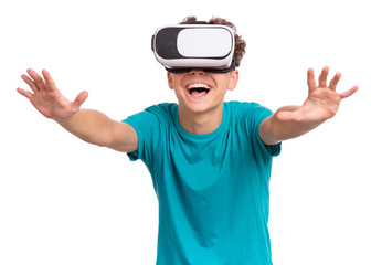 Fototapeta premium Happy teen boy wearing virtual reality goggles watching movies or playing video games. Cheerful smiling teenager looking in VR glasses. Funny child experiencing 3D gadget technology.