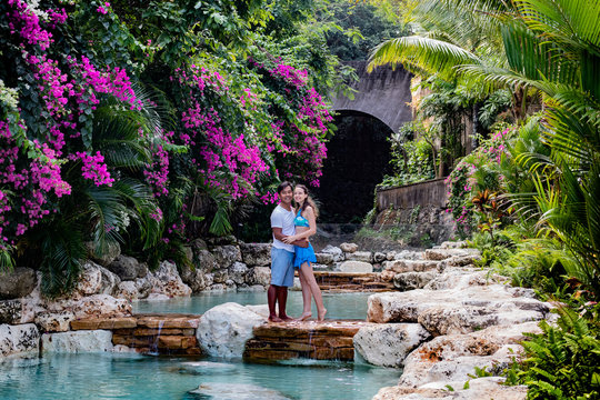 Happy couple on vacation. Multiethnic couple at the swimming pool. Swimming pool surrounded by pink bougainvillea flowers.