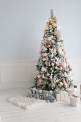 Elegant Christmas tree with white and pink toys and gift boxes in the bedroom of luxury apartments