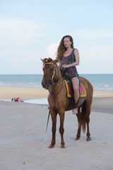 Woman fashion model riding a horse on the beach in summer.