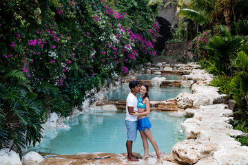 Couple kissing. Multiethnic couple at the swimming pool. Swimming pool surrounded by pink bougainvillea flowers.