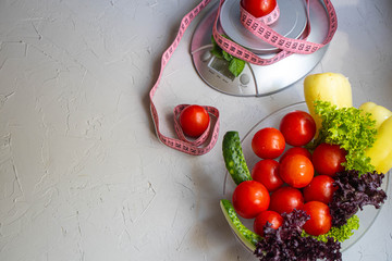 Diet food and measuring tape on a stone background. Cherry tomatoes, lettuce, peppers, cucumbers. Serving Weighing Scales. Concept of diet and healthy lifestyle.