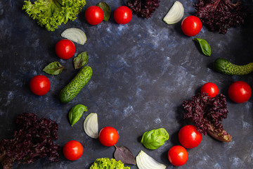 Assorted fresh vegetables. Cherry Tomato, Cucumber, Lettuce, Lettuce, Onion, Basil. All against a dark, stone background. In the middle is a circle unfilled with vegetables. 