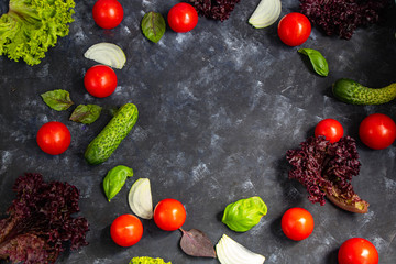 Assorted fresh vegetables. Cherry Tomato, Cucumber, Lettuce, Lettuce, Onion, Basil. All against a dark, stone background. In the middle is a circle unfilled with vegetables. 