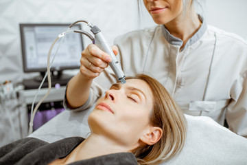 Cosmetologist making vacuum hydro peeling on the forehead region to a woman at the luxury beauty...