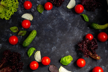 Assorted fresh vegetables. Cherry Tomato, Cucumber, Lettuce, Lettuce, Onion, Basil. All against a dark, stone background. In the middle is a circle unfilled with vegetables. 