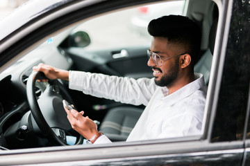 Indian Man sitting in a car and looking at a mobile phone
