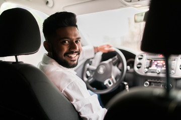 Rear view of young man driving his car looking at camera with smile