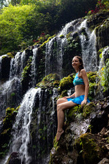 Travel lifestyle. Young traveler woman sitting at waterfall in tropical forest. Banyu Wana Amertha waterfall Wanagiri, Bali, Indonesia.