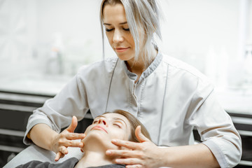 Obraz na płótnie Canvas Cosmetologist making facial massage to a beautiful woman at the beauty salon. Concept of a lymph drainage therapy
