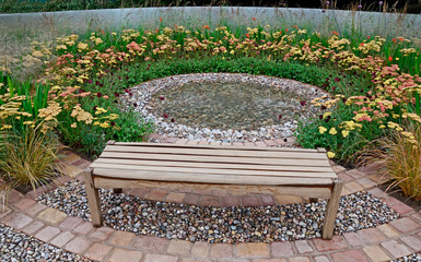 A circular garden design inspired by musical instruments and the abstract sound of a drum with seating, water feature and a border of achillea and grasses © Garden Guru