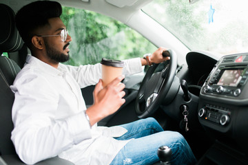 Handsome indian man driving a car with coffee to go