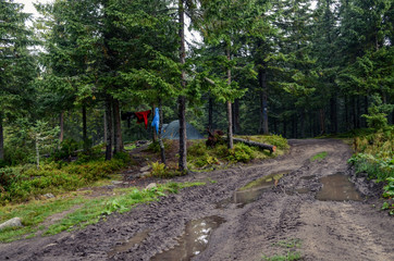 Dirty mountain road with puddles after a thunderstorm go to the tent, next to which dry wet jackets
